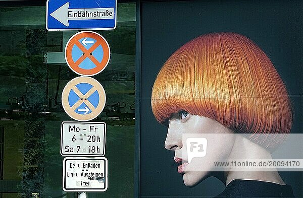 Eine Werbeplakat im Fenster eines Friseursalons zeigt ein Foto einer Frau mit roten Haaren. Es sieht so aus  als würde die Frau auf ein Schilderwald von Verkehrszeichen schauen  17.06.2019