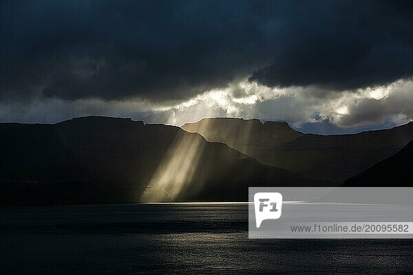 Sonnenstrahlen brechen durch dicke Wolken auf die Küstenlinie der Färöer Inseln