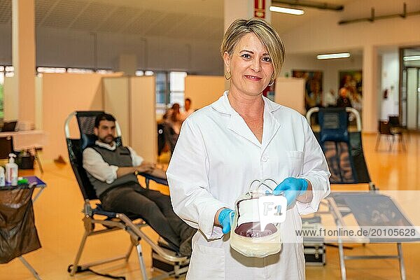 Zufriedene Krankenschwester zeigt einen mit Blut gefüllten Beutel in einem Spendezentrum
