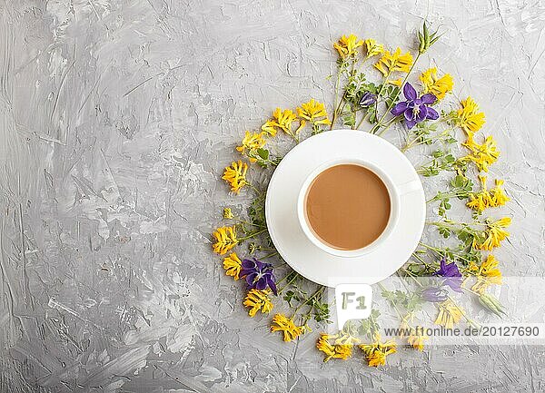Gelbe und blaue Blumen in einer Spirale und eine Tasse Kaffee auf einem grauen Hintergrund aus Beton. Morninig  Frühling  Mode Zusammensetzung. Flachlage  Draufsicht  Kopierraum