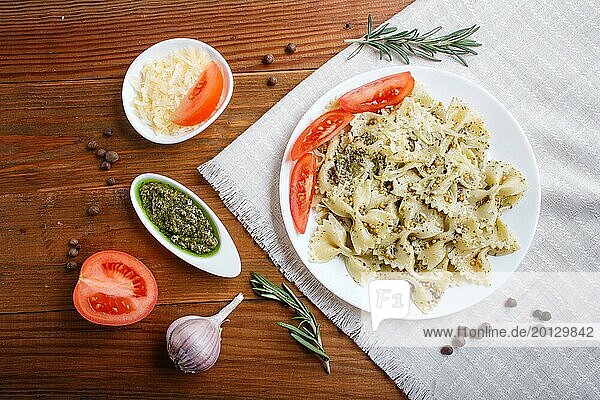 Farfalle pasta with pesto sauce  tomatoes and cheese on a linen tablecloth on brown wooden background. top view  close up