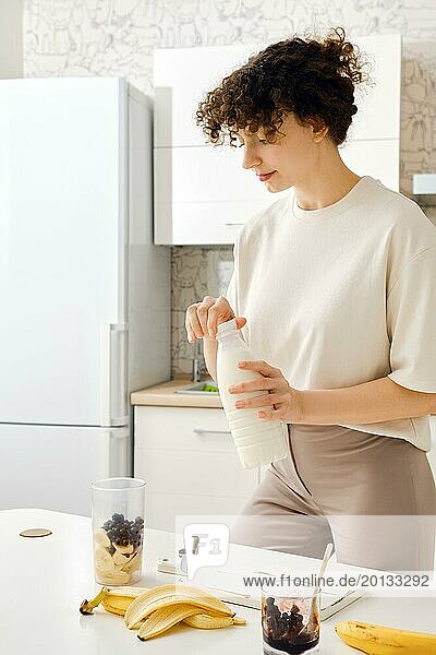 Frau öffnet eine Flasche Milch  um einen Smoothie mit schwarzen Johannisbeeren zu machen