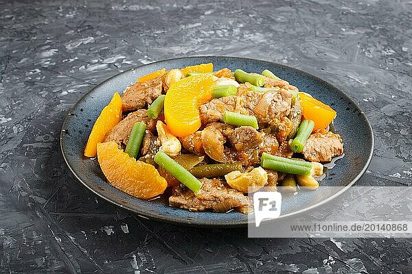 Fried pork with peaches  cashew and green beans on a black concrete background. Side view  close up  chinese cuisine