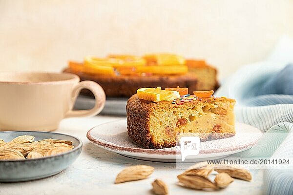Orange cake with almonds and a cup of coffee on a white concrete background and blue linen textile. Top view  close up  selective focus