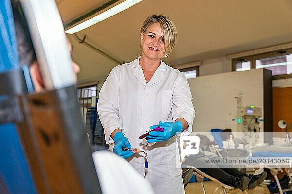 Krankenschwester in Uniform lächelt bei der Blutabnahme von einem Freiwilligen in einem überfüllten Pavillon