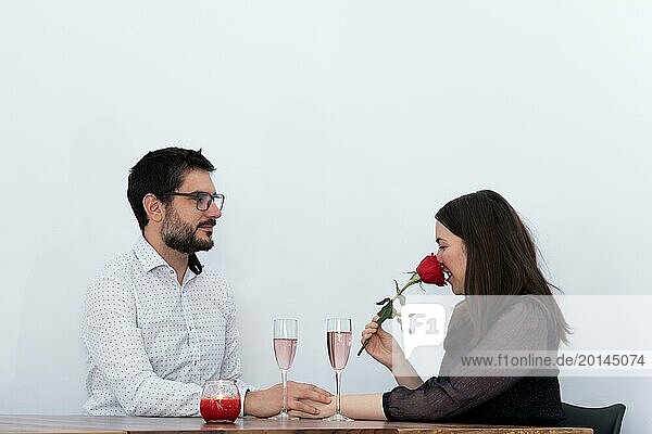 Junge Frau riecht an einer Rose  die ihr ihr Mann geschenkt hat  während sie ein Glas Champagner trinken