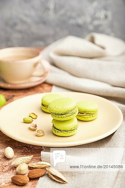 Green macarons or macaroons cakes with cup of coffee on a brown concrete background and linen textile. Side view  close up  selective focus