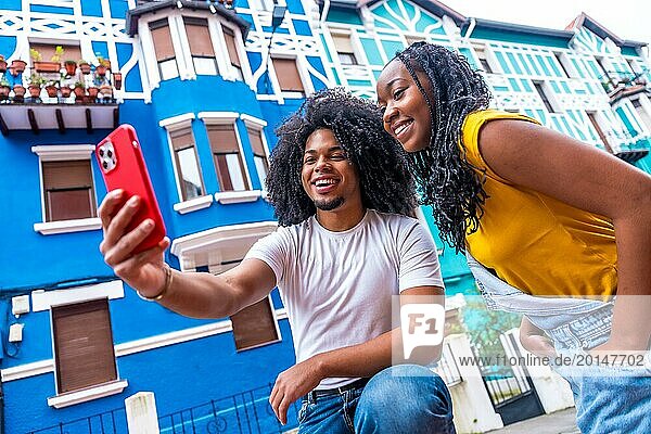 Niedriger Winkel Seitenansicht von zwei jungen afro Freunde nehmen ein Selfie neben bunten Häusern