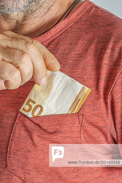 Close-up of man putting euro banknotes in his red T-shirt pocket