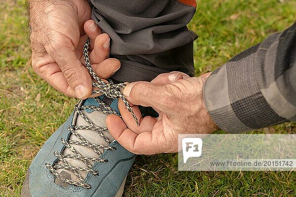 Mann bindet die Schnürsenkel seiner Stiefel auf einer grünen Wiese