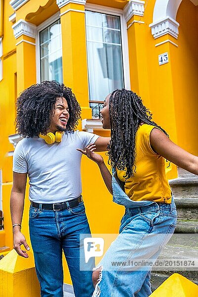 Happy african couple with headphones chilling next to a house with yellow facade