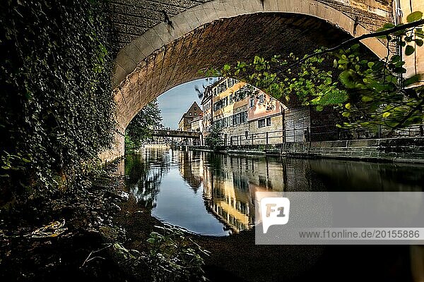 Ein ruhiger Fluss fließt unter einer Brücke durch  mit klaren Spiegelungen der umliegenden Gebäude und Bäume  Alter Hafen am Kanal mit altem Schlachthof in Bamberg von oberer Brücke gesehen