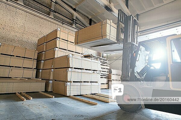 Modern forklift machine moving in warehouse with piles of wooden panels while working on factory