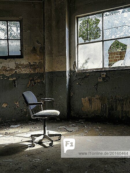 Einzelner Drehstuhl  Bürostuhl in einer leeren verfallenen Fabrikhalle  abblätternde Farbe  Lichteinfall durch kaputte Fensterscheiben  Industrieruine  Innenaufnahme  Lost Place  Deutschland  Europa