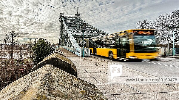 Yellow bus drives past a bridge and wall with motion blur  the atmosphere is dynamic  The blue wonder in Dresden