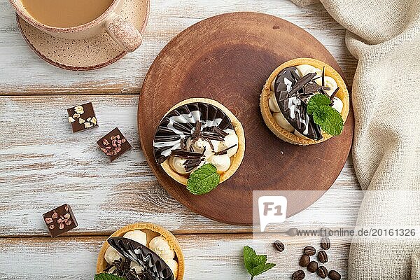 Süße Törtchen mit Schokolade und Käsecreme mit einer Tasse Kaffee auf weißem Holzhintergrund und Leinentextil. Draufsicht  Flachlegung  Nahaufnahme
