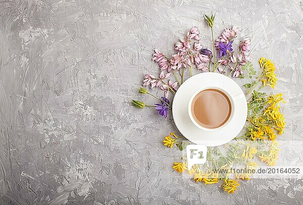 Gelbe  rosa und blaue Blumen in einer Spirale und eine Tasse Kaffee auf einem grauen Hintergrund aus Beton. Morninig  Frühling  Mode Zusammensetzung. Flachlage  Draufsicht  Kopierraum