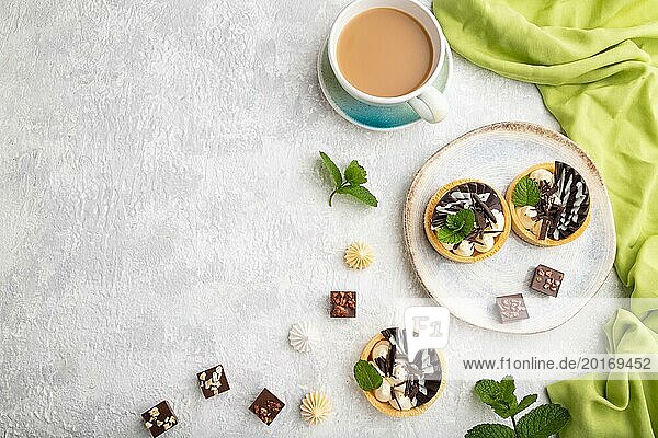 Süße Törtchen mit Schokolade und Käsecreme mit einer Tasse Kaffee auf grauem Betonhintergrund und grünem Textil. Draufsicht  Flat Lay  Copy Space