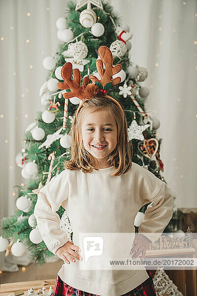 Happy girl standing with hands on hip in front of Christmas tree