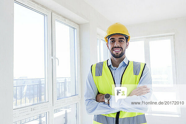 Confident young architect standing with arms crossed at site