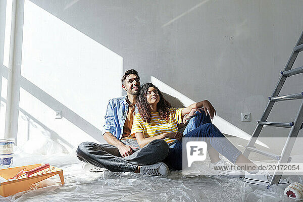 Thoughtful couple sitting near wall at new home