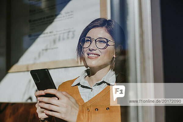 Happy woman using smart phone seen through glass