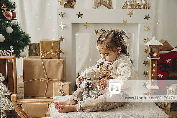 Mädchen spielt mit Schneekugel in der Nähe der Weihnachtsdekoration zu Hause