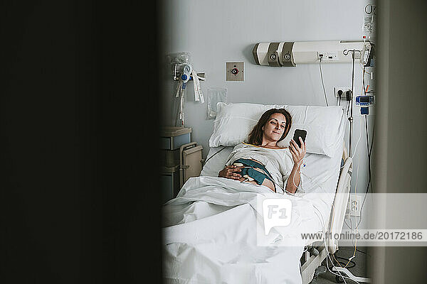 Schwangere Frau liegt im Bett und benutzt Smartphone im Krankenhaus