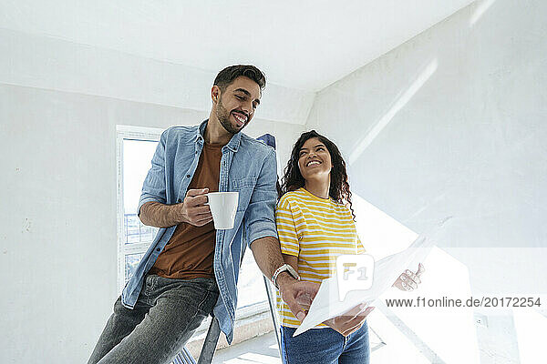 Smiling couple having discussion over blueprint for renovation in new home