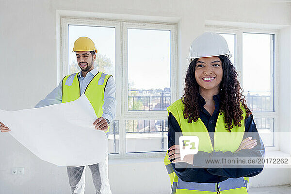 Confident architect standing with arms crossed at site