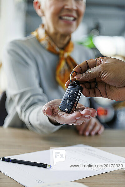 Hand of salesperson giving car keys to woman sitting at desk