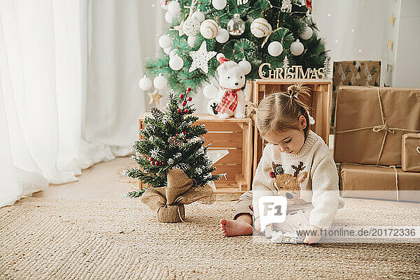 Girl playing with Christmas decoration near tree at home