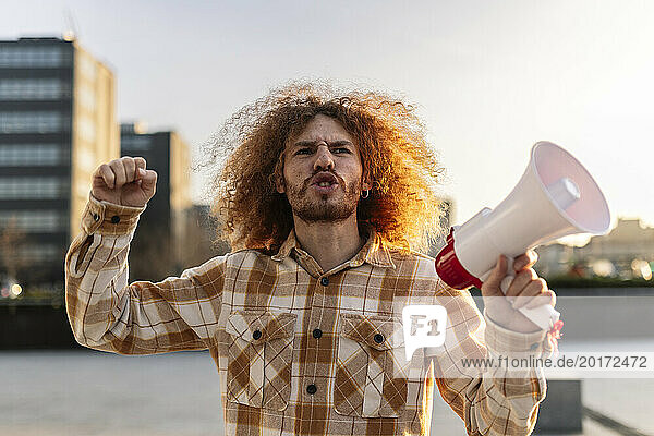 Angry man shouting with megaphone under sky