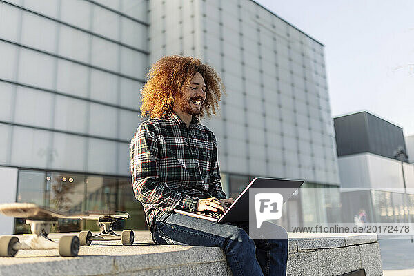 Happy freelancer working on laptop in front of building