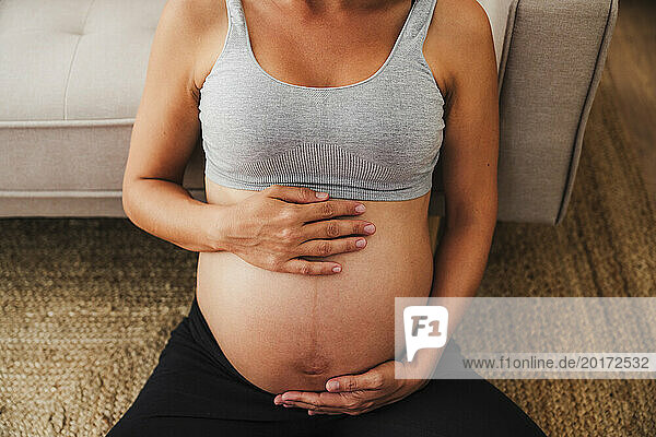Pregnant woman sitting with hands on stomach at home