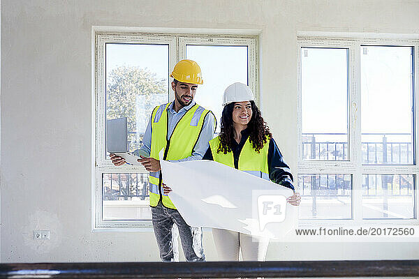 Smiling architects with blueprint and laptop at site