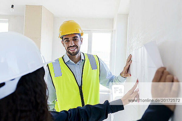 Smiling architect listening to colleague explaining blueprint at site