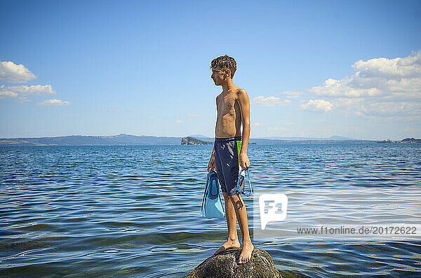 Teenage boy standing on rock in lake Bolsena  Italy