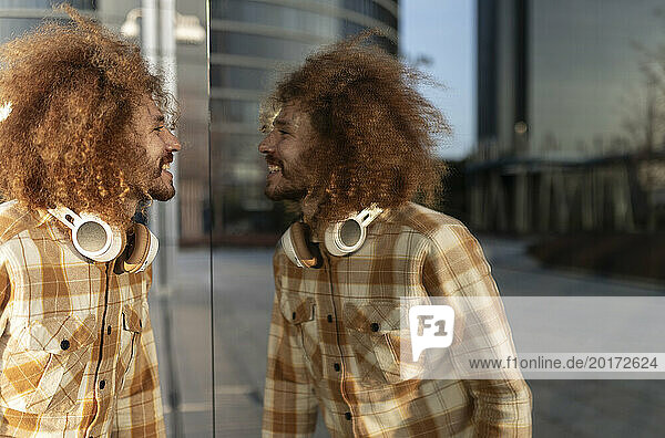 Happy man looking at reflection on glass wall