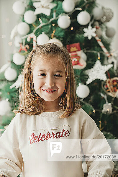 Smiling girl standing in front of Christmas tree at home