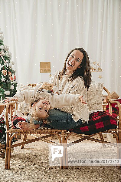Happy mother enjoying with daughter on armchair at home