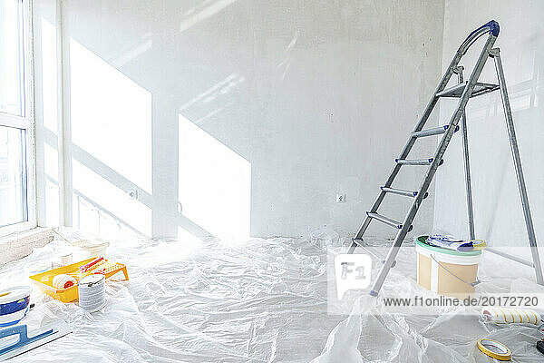 Painting equipment and ladder on floor covered in plastic at home