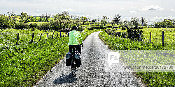 Senior man cycling on road near field on sunny day