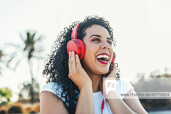 Cheerful woman listening to music through wired headphones at skateboard park
