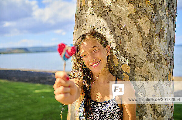 Happy girl holding lollipop near tree trunk