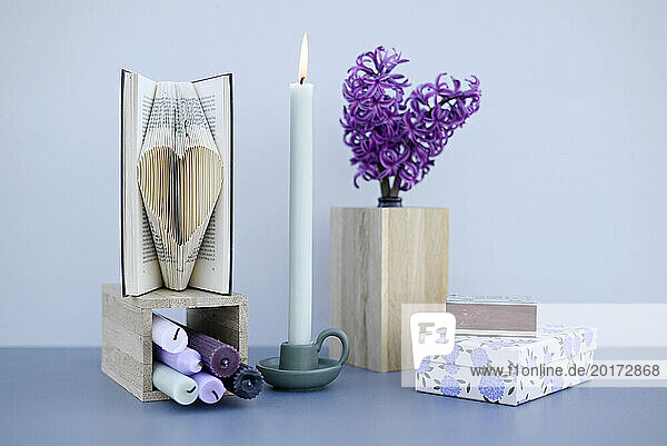 Studio shot of burning candle  blooming hyacinths and heart carved in book pages