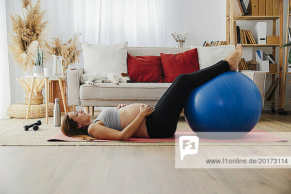 Pregnant woman lying on yoga mat with fitness ball at home