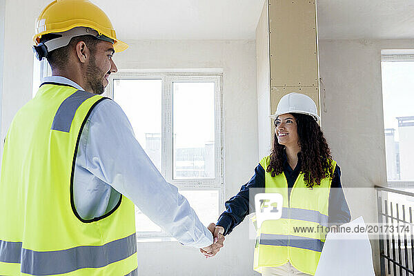 Smiling architect shaking hand with colleague at site