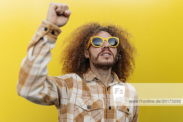 Happy man wearing sunglasses and gesturing in front of yellow wall