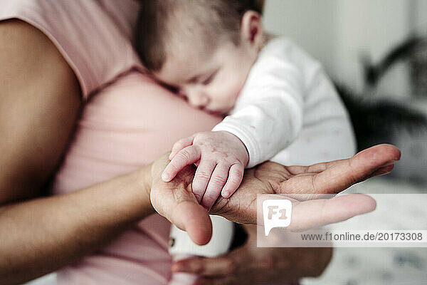 Hand of mother holding baby girl's hand at home